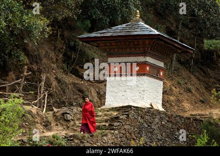 Ein Mönch in rotem Gewand führt einen Felsweg vorbei an kleinen Stätten, während er von Tango Goemba aus spaziert Stockfoto