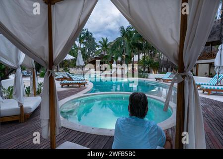 Männlicher Tourist blickt von einer Liege auf einen einladenden Swimmingpool in einem tropischen Resort, Playa del Carmen, Mexiko Stockfoto