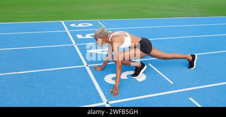 Eine afroamerikanische Athletin steht auf der blauen Olympiastraße an der Startlinie und verkörpert das Konzept des Renntrainings und des Engagements Stockfoto