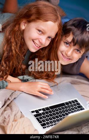 Kinder können sich entspannen und mit einem Laptop auf dem Boden fotografieren, zusammen mit Glücksspielen und Online-Spielen für Urlaub oder Urlaub. Kinder, lächeln und spielen mit Stockfoto