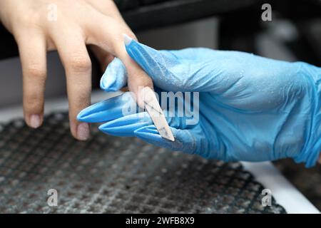 Ein Nageltechniker feilt einen Kantennagel und perfektioniert seine Form. Stockfoto