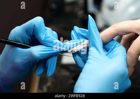 Eine Nahaufnahme eines professionellen Nageltechnikers, der Acrylnägel mit einer elektrischen Handfeile formt und die Präzisionsarbeit in einem Schönheitssalon detailliert beschreibt. Stockfoto