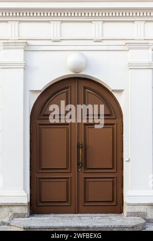 Braune Holzbogentür in weißer Wand mit klassischen Architekturdekorationen, Vorderansicht, Hintergrundfotos Stockfoto