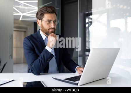 Seriöser junger Geschäftsmann arbeitet konzentriert im Büro an einem Laptop und mit Dokumenten. Stockfoto