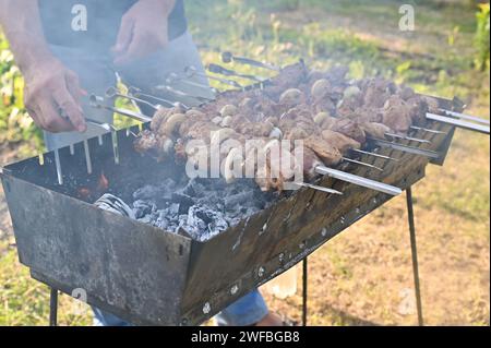 Fleisch auf Spießen wird auf dem Grill gekocht. Ein Mann dreht einen Spieß mit Fleisch um Stockfoto