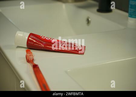 Red colgate Zahnpasta und Zahnbürste auf einer Badezimmertheke in der Nähe des weißen Waschbeckens Stockfoto