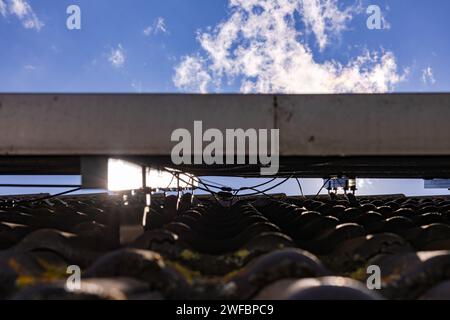 Blick unter einer Photovoltaikanlage mit Befestigung und Kabel auf einem Hausdach mit Dachziegeln in der Hintergrundbeleuchtung Stockfoto