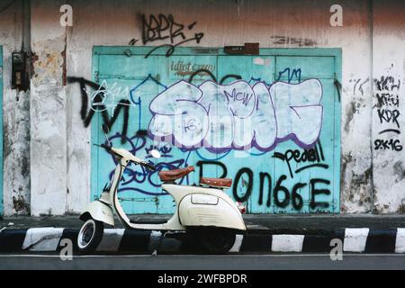 Seitenansicht der klassischen Roller vespa, die auf der Straßenseite mit einer Wand voller Graffiti geparkt ist Stockfoto