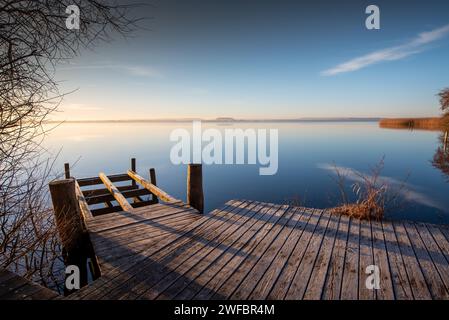 Fußgängerbrücke oder Steg bei Sonnenaufgang bei frostigem Wetter vor einem ruhigen, spiegelglatten See. Meditativer Blick über das Steinhuder Meer. Stockfoto