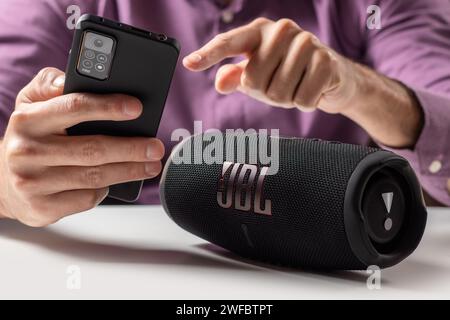 Dnioro Ukraine. 27. januar 2023: Mann hält Smartphone und verwendet tragbaren Musiklautsprecher JBL Charge 5. Stockfoto