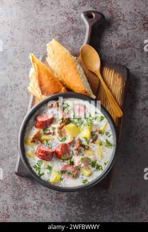 Polieren Sie weißen Borschtsch mit Gemüse, Räucherwurst, getrockneten Pilzen und Speck in Nahaufnahme auf einem Teller auf dem Tisch. Vertikale Draufsicht von oben Stockfoto