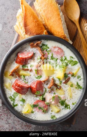 Polnische Zalewajka-Suppe auf Roggensauerteig mit Wurzelgemüse, geräucherter Wurst, getrockneten Pilzen und Speck in Nahaufnahme auf einem Teller auf dem Tisch. Vertikal oben Stockfoto