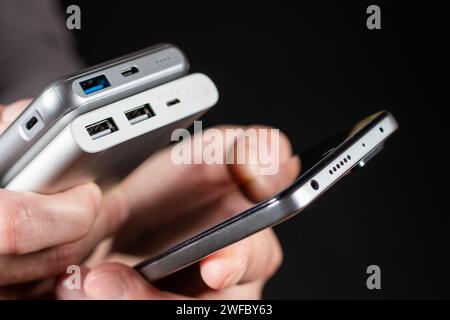 Der Mann hält Telefon und Ladegerät in der Hand. Powerbank und Smartphone in der Hand. Stromspargerät Powerbank Smartphone Stockfoto