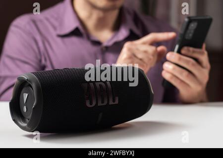 Dnioro Ukraine. 27. januar 2023: Mann hält Smartphone und verwendet tragbaren Musiklautsprecher JBL Charge 5. Stockfoto