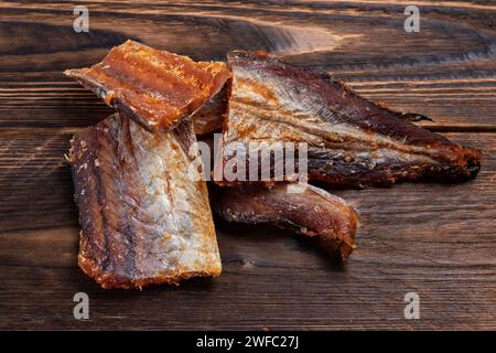 Stücke von gereinigtem getrocknetem Fisch auf hölzernem Hintergrund. Trocken Gewürzter Pollack. Bernstein mit Pfeffer. Stockfoto