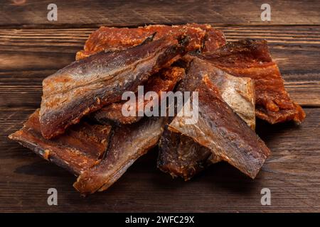 Stücke von gereinigtem getrocknetem Fisch auf hölzernem Hintergrund. Trocken Gewürzter Pollack. Bernstein mit Pfeffer. Stockfoto