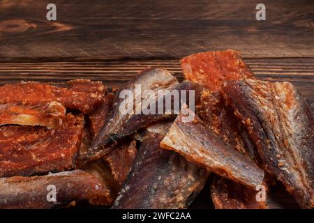 Stücke von gereinigtem getrocknetem Fisch auf hölzernem Hintergrund. Trocken Gewürzter Pollack. Bernstein mit Pfeffer. Stockfoto