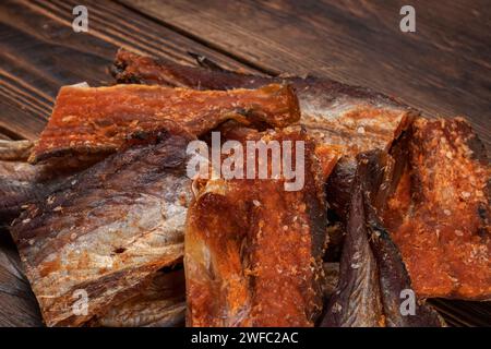 Stücke von gereinigtem getrocknetem Fisch auf hölzernem Hintergrund. Trocken Gewürzter Pollack. Bernstein mit Pfeffer. Stockfoto