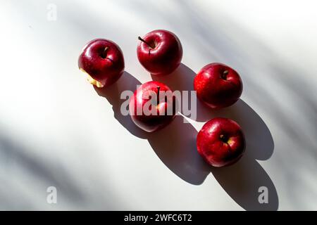 Fünf rote reife Äpfel liegen auf einem weißen Tisch und ihre Schatten Stockfoto