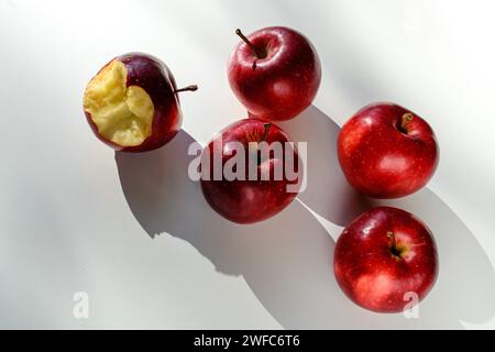 Fünf rote reife Äpfel liegen auf einem weißen Tisch und ihre Schatten Stockfoto