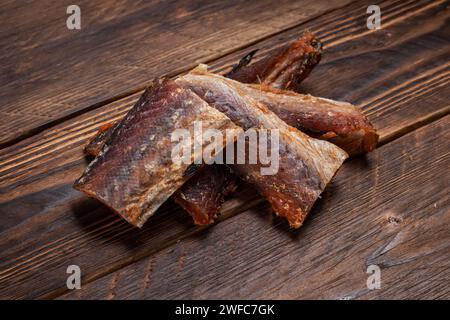 Stücke von gereinigtem getrocknetem Fisch auf hölzernem Hintergrund. Trocken Gewürzter Pollack. Bernstein mit Pfeffer. Stockfoto