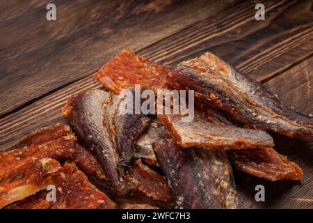 Stücke von gereinigtem getrocknetem Fisch auf hölzernem Hintergrund. Trocken Gewürzter Pollack. Bernstein mit Pfeffer. Stockfoto