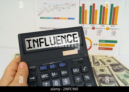 Geschäftskonzept. Auf dem Tisch stehen Finanzberichte, Dollar, in den Händen eines Taschenrechners mit der Inschrift - EINFLUSS Stockfoto