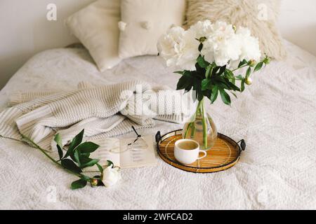 Offenes Buch mit Gläsern, Tasse Kaffee und Blumenstrauß mit weißen pinkfarbenen Pfingstrosen Stockfoto