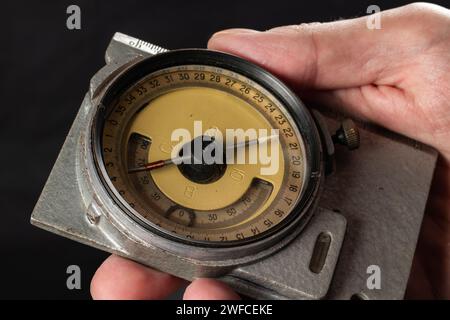 Alter Bergbaukompass in der Hand auf dunklem Hintergrund aus nächster Nähe. Stockfoto