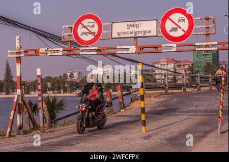 Eine Cham oder Muslimin fährt mit ihrem Motorrad durch den Eingang zur alten Französischen Brücke auf dem Praek Tuek Chhu Fluss. Kampot, Kambodscha. © Kraig Lieb Stockfoto