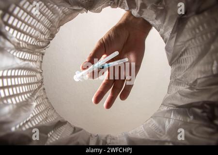 Wirft die Spritze mit der Packung von Hand in den Papierkorb. Innenansicht. Stockfoto