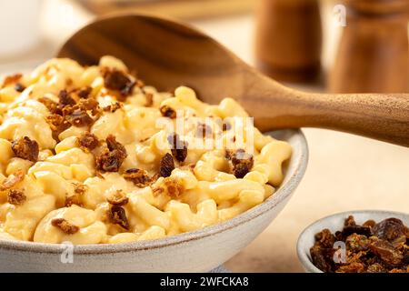 Großaufnahme von Makkaroni und Käse mit Speckstücken in einer weißen Servierschale und Holzlöffel Stockfoto