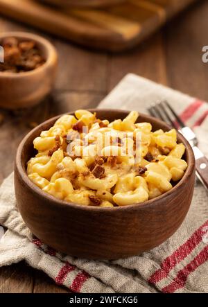 Makkaroni und Käse mit Speckstücken in einer Holzschale auf einem Handtuch und rustikalem Holztisch Stockfoto