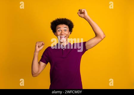 Foto des überfröhlichen Mannes trägt magentafarbene trendige Kleidung hebt die Hände, die den Sieg auf gelbem Hintergrund feiern Stockfoto