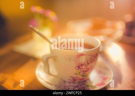 Tasse Tee auf eine Untertasse und Löffel. Warmes Licht im Zimmer. Gemütliche Atmosphäre Stockfoto