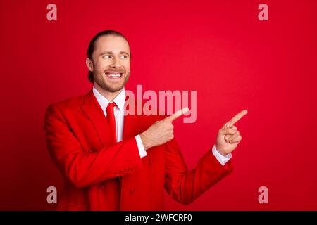 Foto-Porträt des eleganten jungen männlichen Punktausblicks fröhlicher leerer Raum tragen trendige klassische Kleidung isoliert auf rotem Farbhintergrund Stockfoto