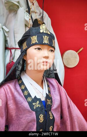 Eine Ausstellung alter, traditioneller, zeremonieller Kleidung, getragen von jemandem koreanischer Abstammung. Ein junges Mädchen in violettem Gewand und schwarzem Kopfschmuck. An der zentralen S Stockfoto