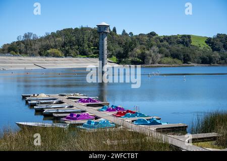 Ruderboote und Tretboote an einem Dock mit Blick auf den Einlassturm am Lafayette Reservoir an einem klaren Tag, Lafayette, Kalifornien, 24. März 2023. Stockfoto