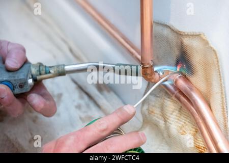Ein Klempner, der Kupferrohre mit einem Lötbrenner erhitzt. Der Heizungsingenieur verbindet zwei Rohre mit geschmolzenem Löt über eine Winkelverbindung. Stockfoto