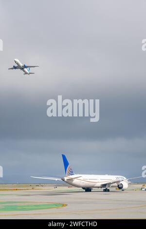 Ein United Airlines Jet Taxis auf dem Asphalt, während ein weiterer Jet an einem bewölkten Tag am San Francisco International Airport, San Francisco, Kalifornien, am 11. März 2023 über dem Boden abhebt. Stockfoto