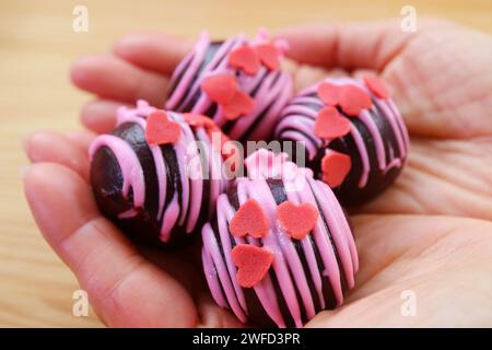 Köstliche Schokoladenkuchen-Pops mit herzförmiger Erdbeer-Royal-Glasur in der Hand Stockfoto