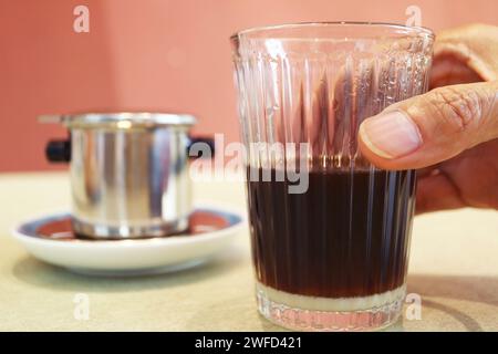Nahaufnahme einer Hand, die ein Glas frisch gebrühten vietnamesischen Tropfkaffee hält Stockfoto