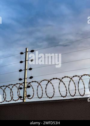 Elektrischer Sicherheitszaun an einer Wand mit einem dramatischen Himmel im Hintergrund. Stockfoto