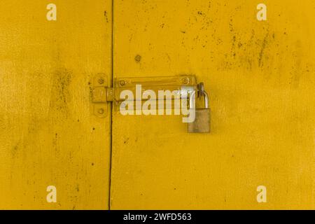 Vorhängeschloss auf gelbem Holztor, der einen strukturierten Hintergrund bildet. Stockfoto