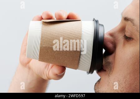 Mann trinkt aus Pappbecher Seitenansicht nah oben isoliert auf weißem Studio Hintergrund Stockfoto