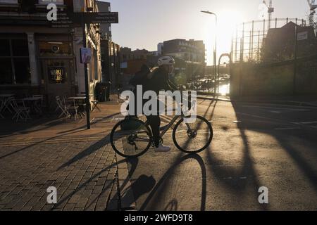 Eine weiße Fahrradfahrerin pendelt in der frühen Morgensonne. Sie ist teilweise in der Sonne geschildert und wirft einen Schatten auf die Straße. Stockfoto