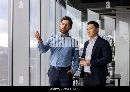 Zwei männliche Unternehmensexperten diskutieren in ihrem gut beleuchteten Büro ernsthaft über Geschäftsstrategien. Stockfoto