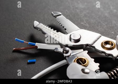 Entfernen der Isolierung vom Leiter mit einem Werkzeug. Abisolierwerkzeug auf dunklem Hintergrund. Stockfoto