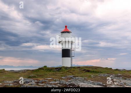 Der Leuchtturm von Borhella steht stark vor einem dramatischen Himmel, seine rote Kappe bildet einen starken Kontrast zu den stimmungsvollen Wolken über der norwegischen Küste Stockfoto