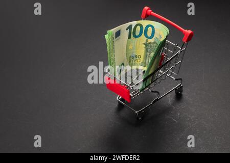 Einkaufswagen mit 100 Euro-Banknoten auf schwarzem Hintergrund, die Währung kaufen. Währungsumtausch. Weltfinanzkrise. Inflation in Europa. Euro Stockfoto